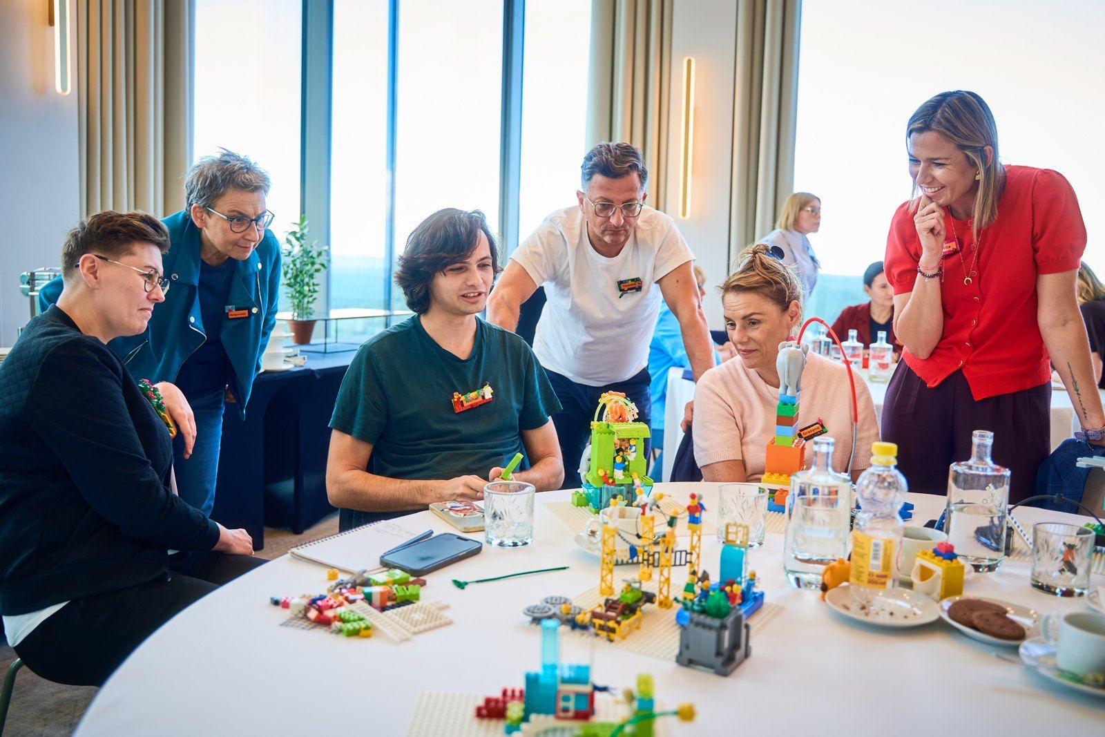Sześcioro uczestników przy wspólnym stole omawia liczne modele z klocków LEGO