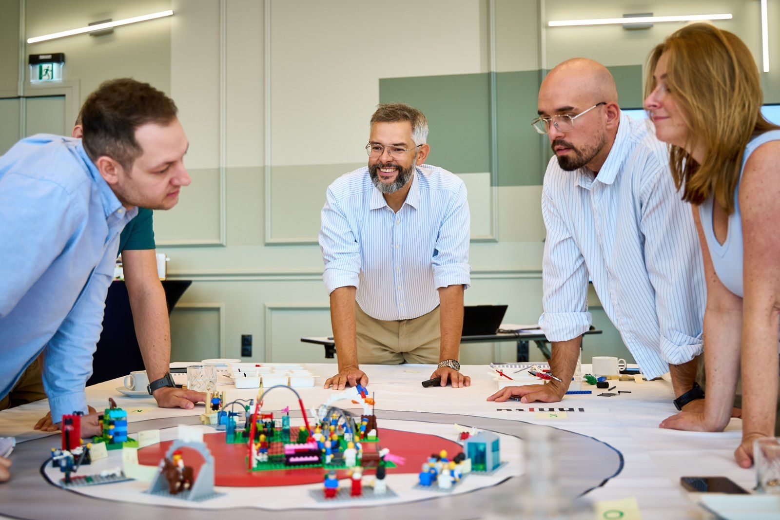 Kilka osób przy wspólnym stole ogląda zbudowane modele z klocków LEGO