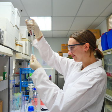 A student in a lab coat and glasses putting something in a vial on an internship in Thailand.