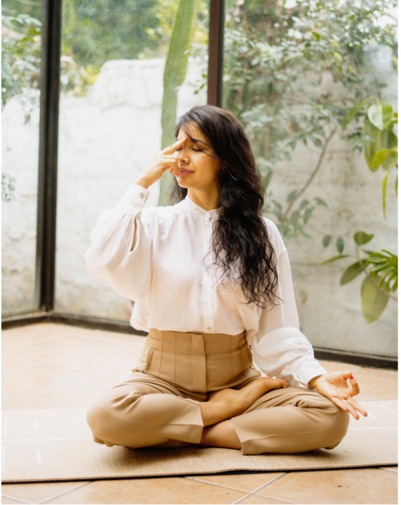 Mujer en blanco practicando pranayama sentada con las piernas cruzadas entre plantas