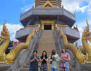Three students with their Resident Director in front of a traditional Thai Wat in Thailand.