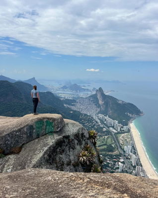 A student standing on top of a mountain overlooking the city and ocean.