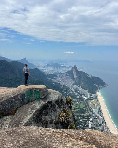 A student standing on top of a mountain overlooking the city and ocean.