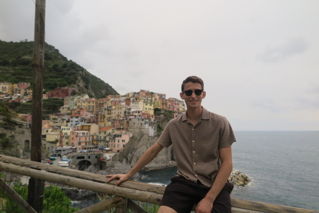 Aiden sitting on a railing with historic buildings and the sea behind him while studying abroad in Viterbo, Italy.